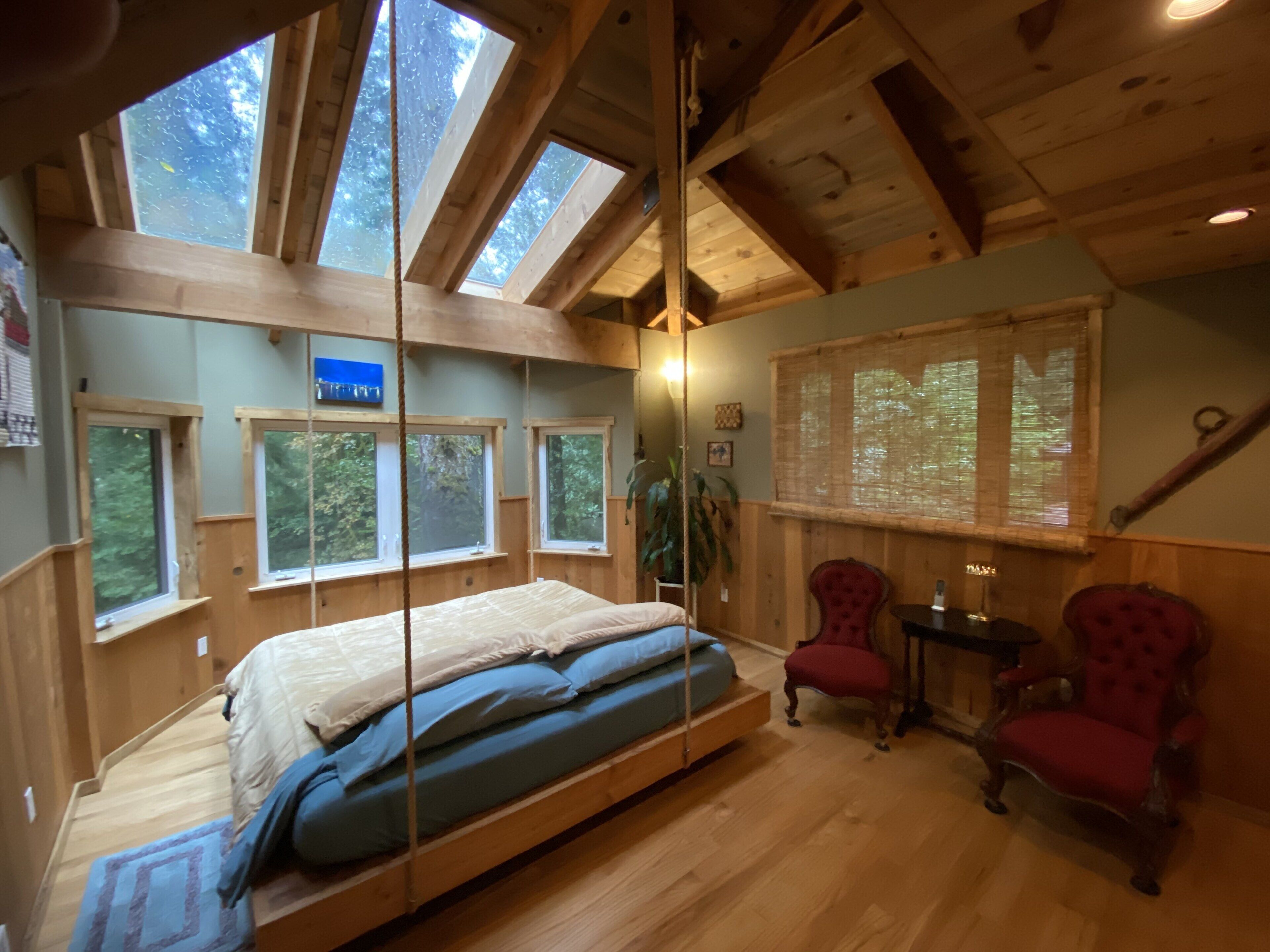 Une chambre confortable avec un lit en mezzanine, des poutres en bois, de grandes fenêtres et un fauteuil rouge.