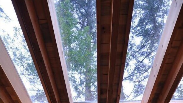 Una tienda de campaña con tragaluz, vigas de madera y ventana con vistas a un bosque.