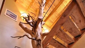 Un interior de madera con una escultura original de un árbol, vigas de madera y una escalera.