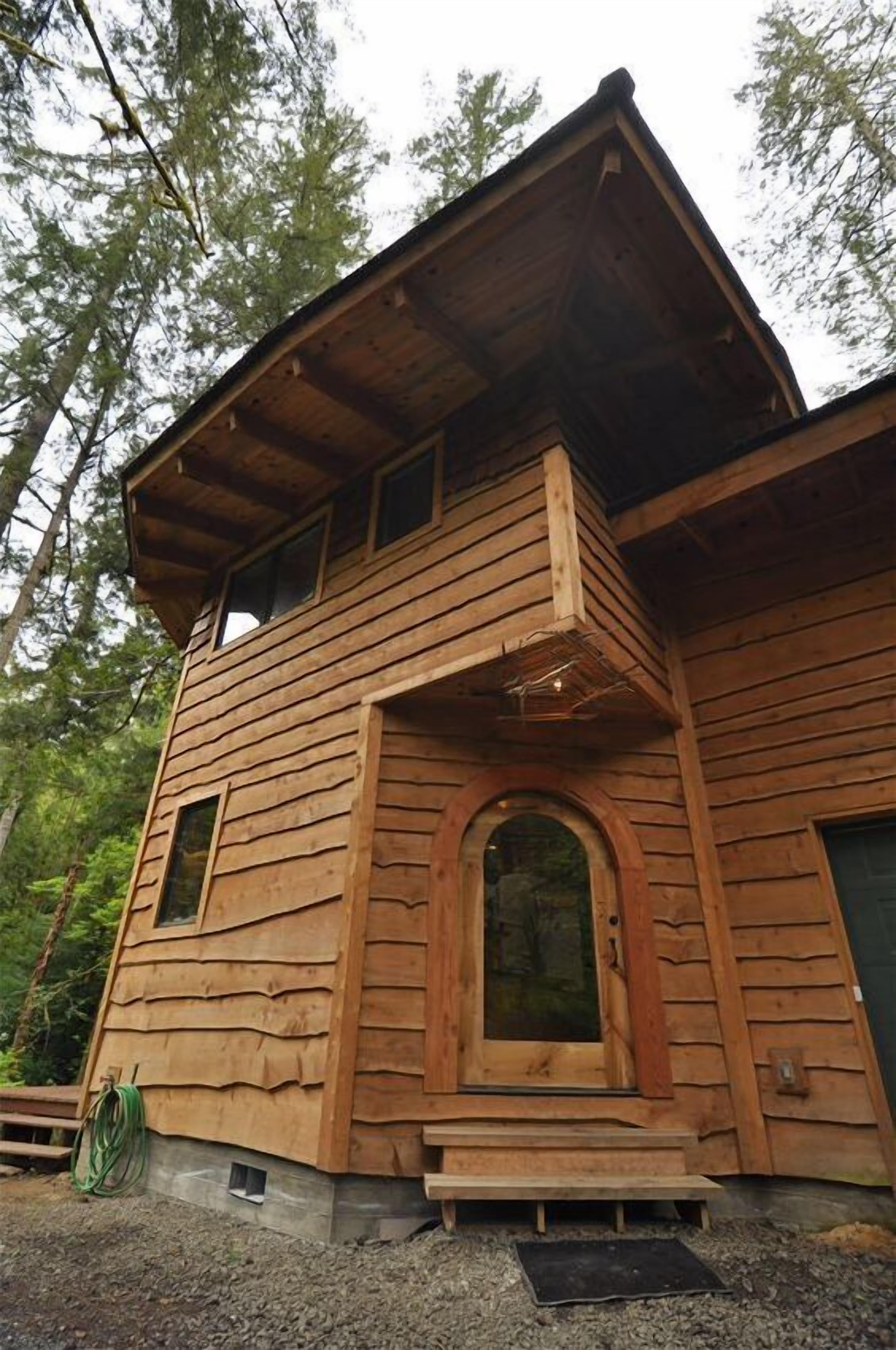 Una cabaña de madera con techo inclinado, una puerta central arqueada y un pequeño porche.