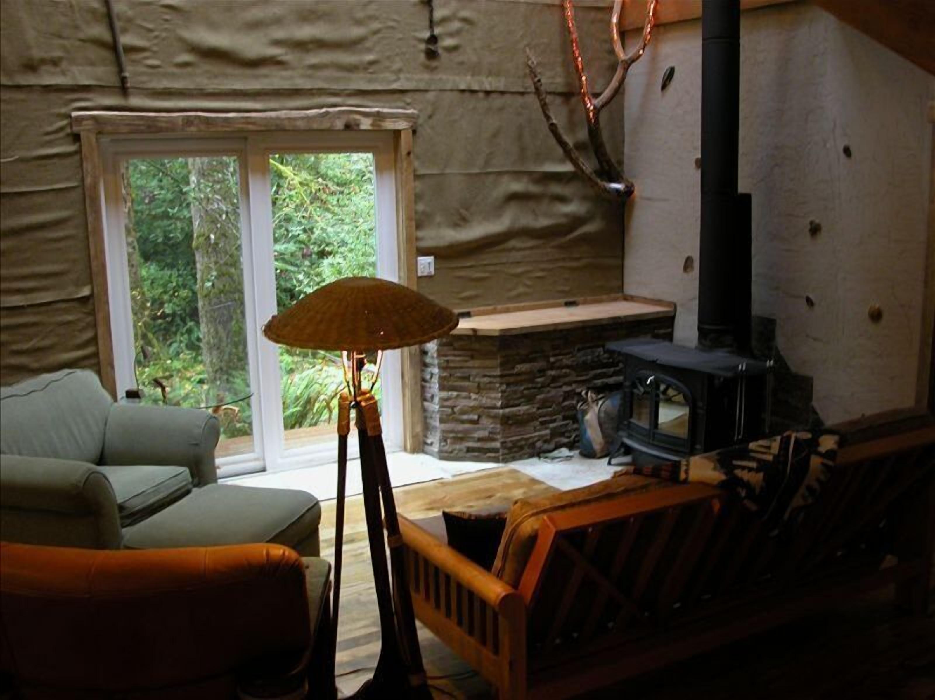 Ein gemütliches Blockhaus-Interieur mit Kamin aus Stein, einer Couch und einem großen Fenster mit Blick auf viel Grün.