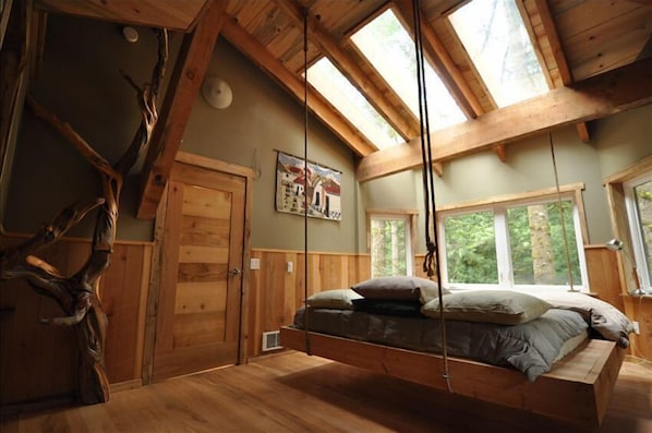Una habitación rústica de madera con cama en entrepiso, ventanas amplias y una decoración con tronco de árbol.