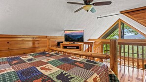 Un dormitorio acogedor con techo de madera, colcha acolchada, ventilador de techo y televisor sobre un soporte de madera.
