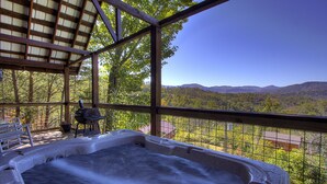 Un jacuzzi con una terraza de madera y vistas a un bosque y montañas.
