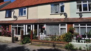 A two-story house with a red-tiled roof, satellite dishes, and a front garden with flowers.