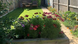 A residential backyard with a lawn, flower beds, a wooden bench, and a brick house with a tiled roof.