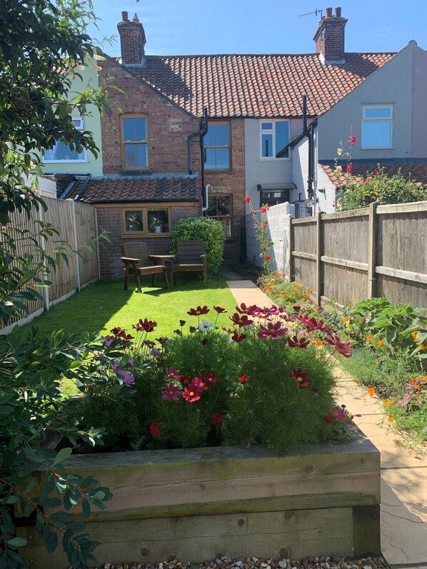 A residential backyard with a lawn, flower beds, a wooden bench, and a brick house with a tiled roof.