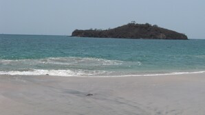 Uma praia com águas turquesa cristalinas e uma pequena ilha ao longe.