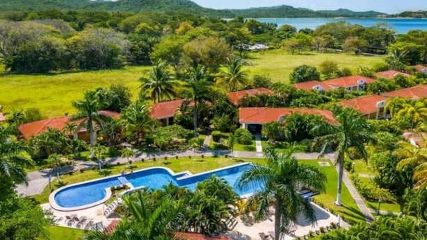 Vista aérea de um resort com piscina, vegetação exuberante e vista para o mar.