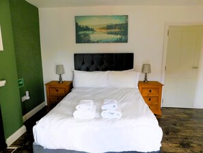 A hotel room with a large bed, two bedside tables with lamps, a painting on the wall, and a green accent wall. - Westbrook, Regis Place - A delightfully modernised period, former fisherman’s semi-detached cottage (Sheringham)