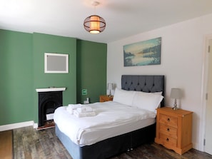 A bedroom with a bed, nightstands, a lamp, a fireplace, and a painting on the wall.