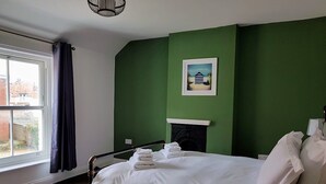 A bedroom with a bed, a fireplace, a window with curtains, and a green wall. - Westbrook, Regis Place - A delightfully modernised period, former fisherman’s semi-detached cottage (Sheringham)