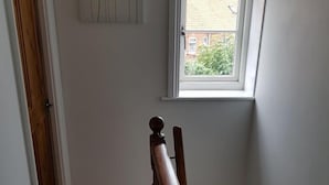 A staircase with a wooden handrail leading to a window with a view of greenery outside. - Westbrook, Regis Place - A delightfully modernised period, former fisherman’s semi-detached cottage (Sheringham)