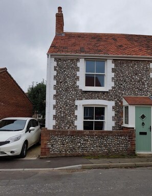 A two-story house with a stone facade, a red-tiled roof, and a green door.