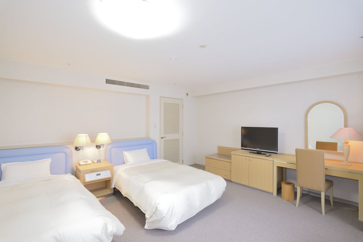 Ein Hotelzimmer mit zwei Betten, einem Schreibtisch, einem Fernseher und einem Spiegel.