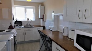 Una cucina moderna con mobili bianchi, forno integrato, microonde e bollitore.
