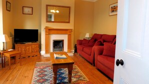A living room with a fireplace, a television, a sofa, and a patterned rug. - The Prairie -  a deceptively spacious cottage with parking close to the beach in Sheringham (Sheringham)