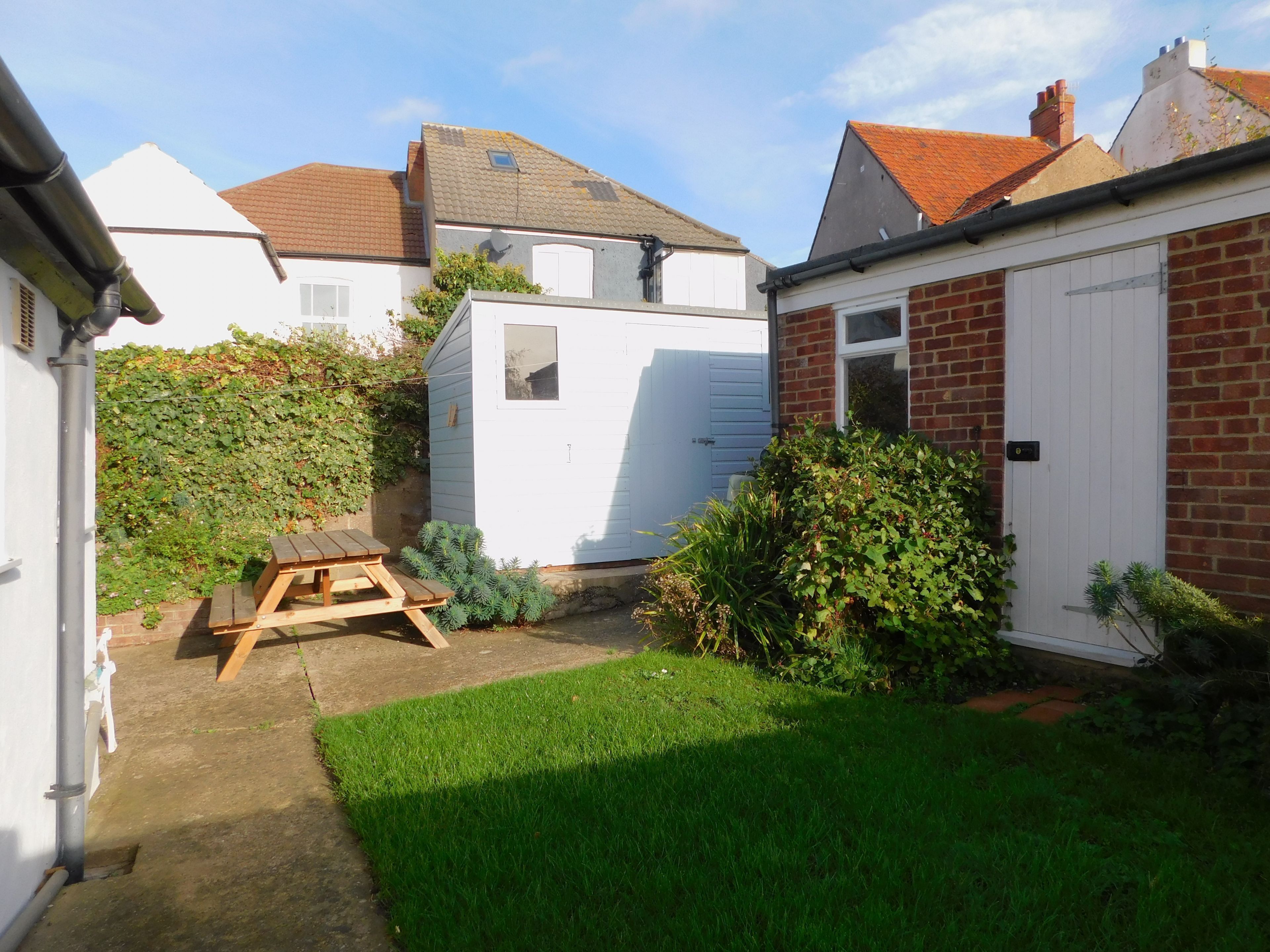 A backyard with a wooden picnic table, a white shed, and a brick house.