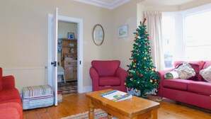 A living room with a wooden coffee table, a red armchair, a sofa, a Christmas tree, and a patterned rug. - The Prairie -  a deceptively spacious cottage with parking close to the beach in Sheringham (Sheringham)