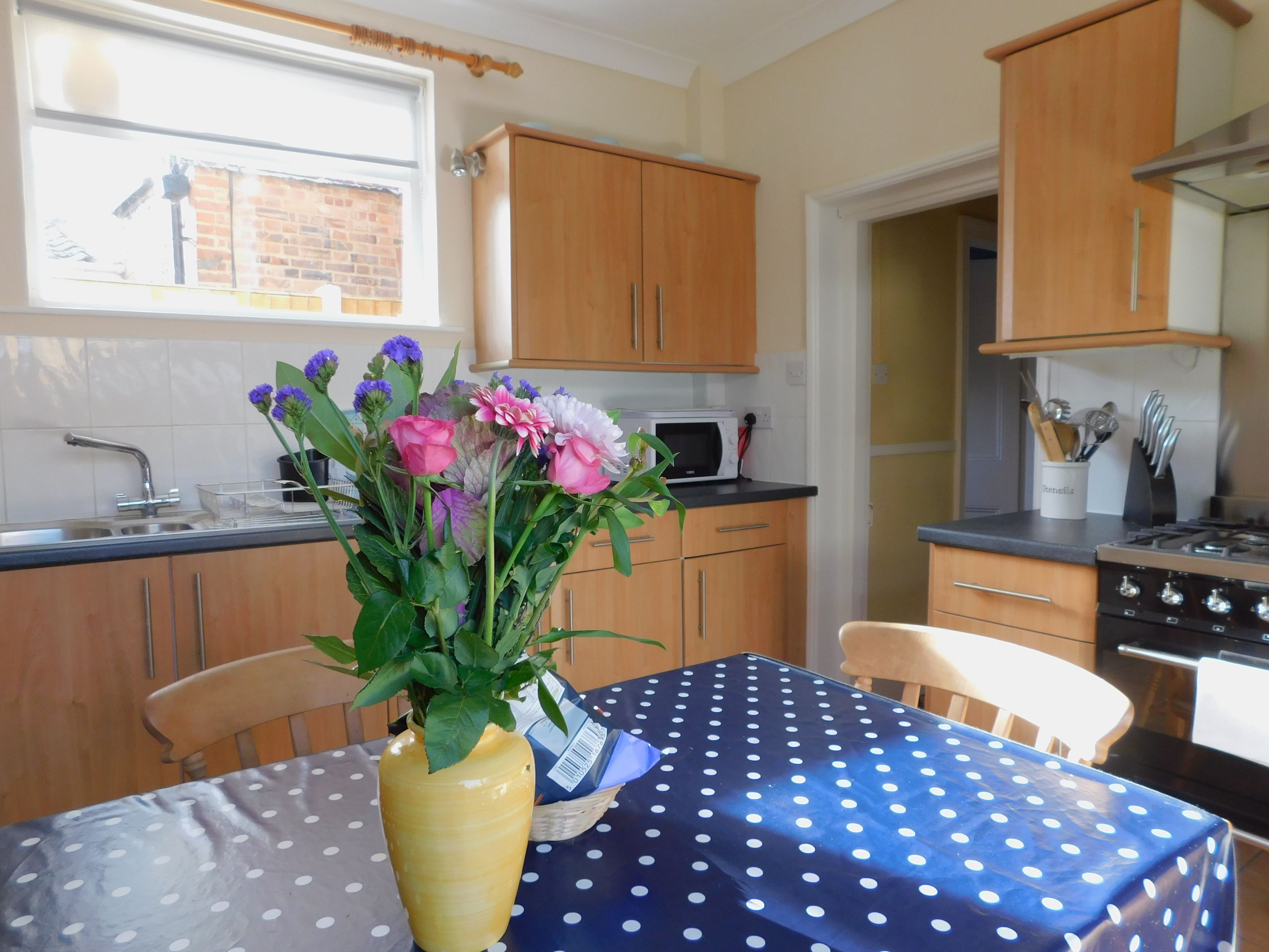 A kitchen with wooden cabinets, a microwave, and a stove. There is a vase with flowers on the table.