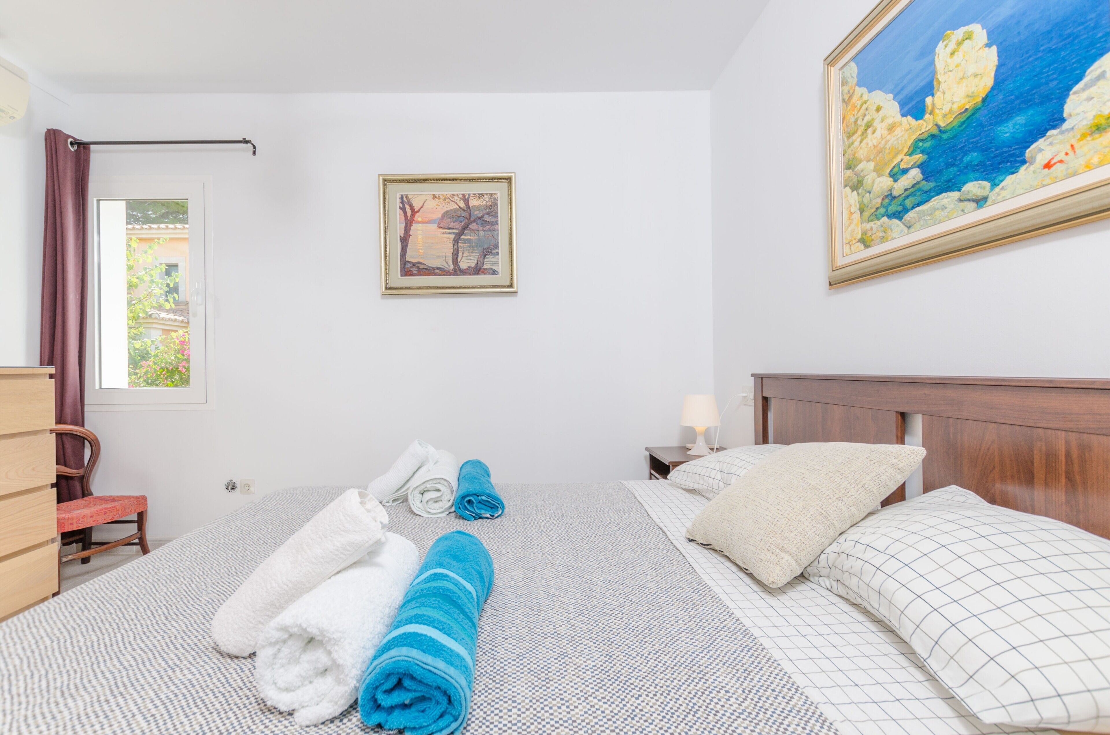 Ein Hotelzimmer mit einem Bett, zwei Kissen, einem Nachttisch mit Lampe, einem Sessel, einem Schminktisch und einem Fenster mit Vorhängen. An der Wand hängt ein Gemälde.