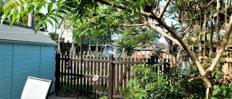 Un pati amb una tanca de fusta, una caseta blava i una zona de terrassa amb una cadira.