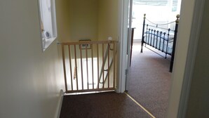 A hallway with a wooden gate leading to a bedroom with a metal bed frame. - Poppy Cott - traditional cottage with stunning views over Beeston Common, the perfect retreat. (Sheringham)