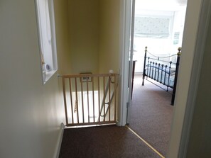 A hallway with a wooden gate leading to a bedroom with a metal bed frame.