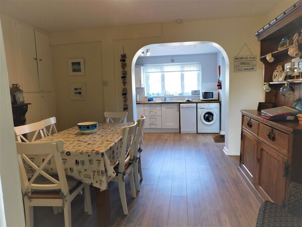 A compact kitchen with a dining area, featuring a washing machine, a microwave, and a dining table with chairs.