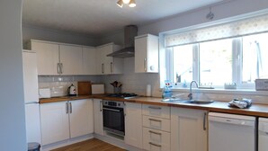 Une cuisine moderne avec des armoires blanches, un plan de travail en bois, une cuisinière, un four, un lave-vaisselle et une fenêtre donnant sur l’extérieur.