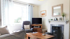 Un salon comprenant un canapé, un fauteuil, une table basse en bois, un téléviseur, une cheminée et une fenêtre avec des rideaux.