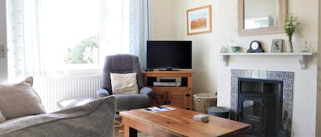 Un salon comprenant un canapé, un fauteuil, une table basse en bois, un téléviseur, une cheminée et une fenêtre avec des rideaux.
