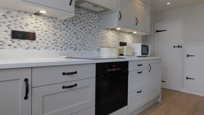 Ett modernt kök med vita skåp, en svart ugn och en mikrovågsugn placerad på bänkskivan.