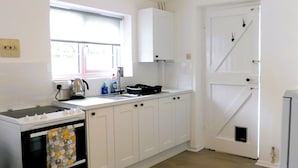 A kitchen with white cabinets, a window, a sink, a stove, and a ceiling light fixture. - In a quiet street this pretty bungalow is located close to the beach & the town centre of Sheringham (Sheringham)