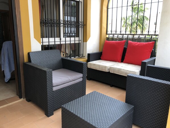 Un patio amueblado con mobiliario de mimbre, incluyendo un sofá y dos sillones, junto a una pequeña mesa.