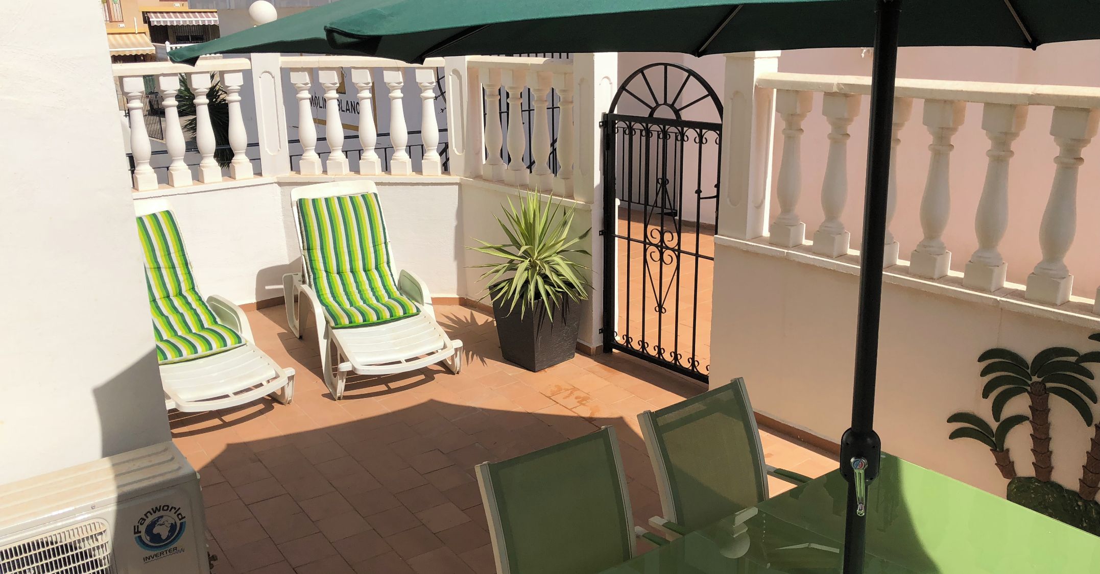 A balcony with two striped lounge chairs, a potted plant, and a glass table.