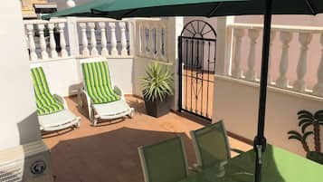 A balcony with two striped lounge chairs, a potted plant, and a glass table.