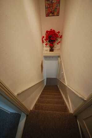 A carpeted staircase with a white wall and a small table with a vase of red flowers at the top.