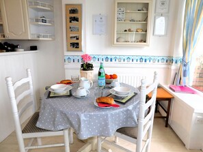 Comedor con una mesa preparada para dos personas, sillas, un jarrón con flores y una estantería con adornos.