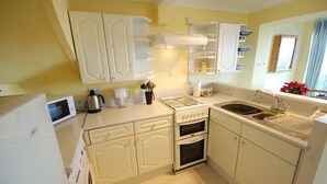 Una cocina compacta con armarios blancos, estufa, horno, microondas y pileta.