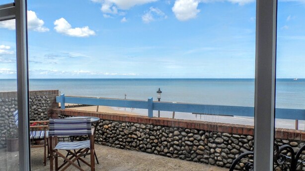 Un balcón con vista al mar, un muro de piedra y una mesa con sillas.