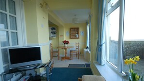 Habitación acogedora con televisor, una pequeña mesa de comedor y sillas. Se ve un ventanal con vistas al exterior.
