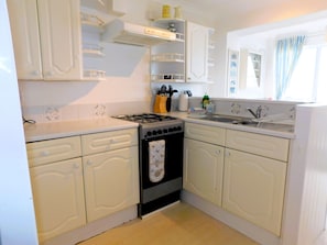 A kitchen with white cabinetry, a gas stove, a sink, and a window with curtains.