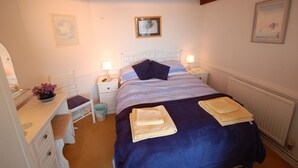 Un dormitorio con una cama, dos mesitas de noche, un tocador, una silla, un aparador y un radiador.