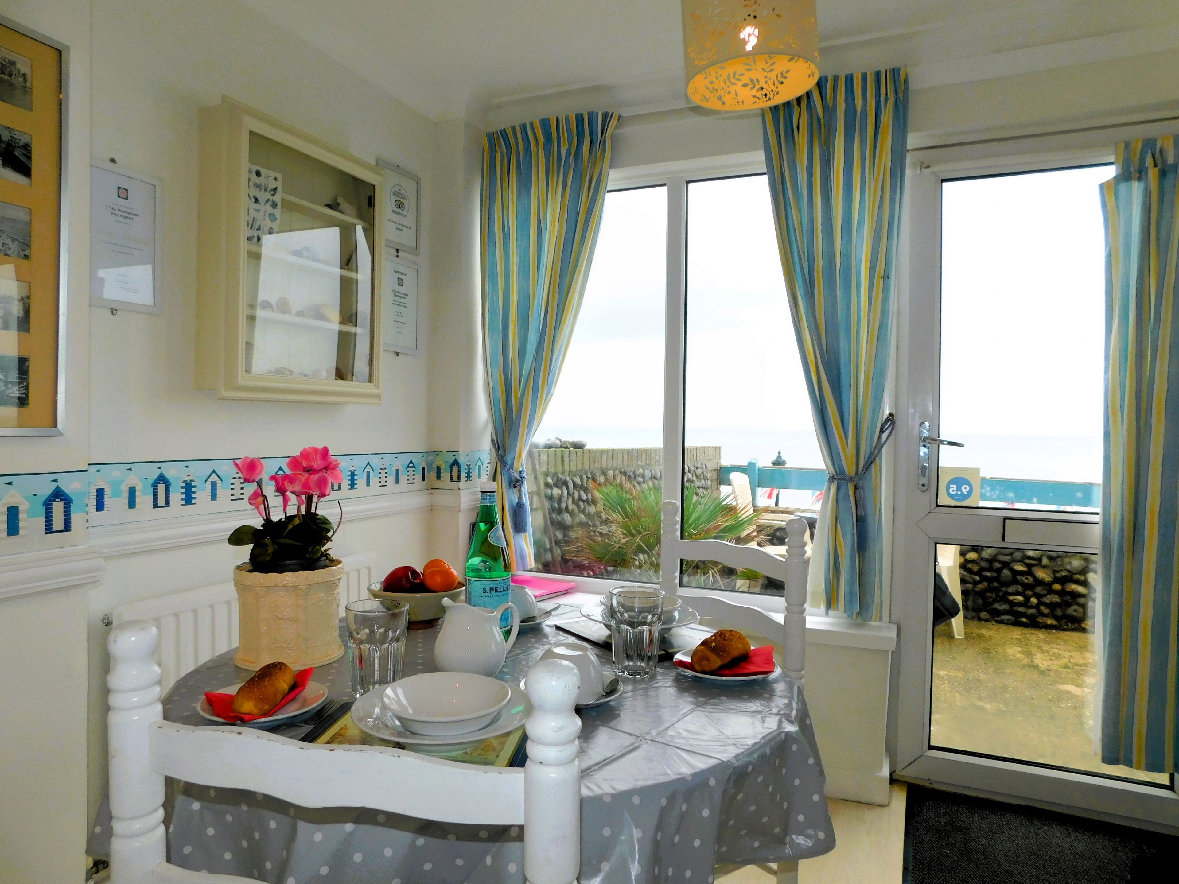 A dining area with a table set for two, a view of the sea through large windows, and a balcony with a view of the beach.