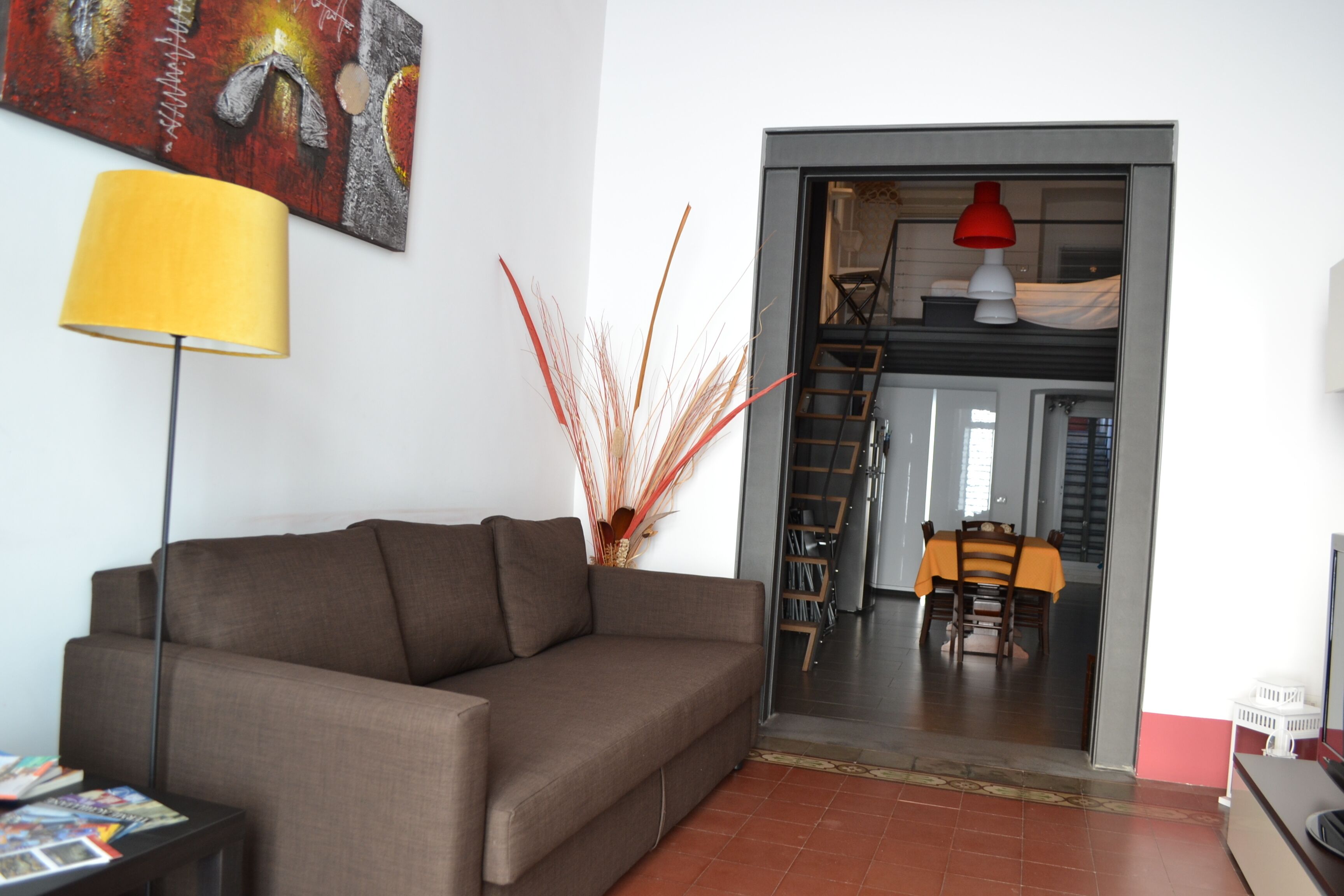 A living room with a brown sofa, a yellow floor lamp, and a painting on the wall.