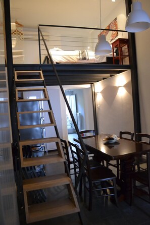 A loft-style room with a wooden ladder leading to a loft bed, a dining table with chairs, and pendant lighting. - Loft in the center of Catania for 2 + 2 people (Catania)