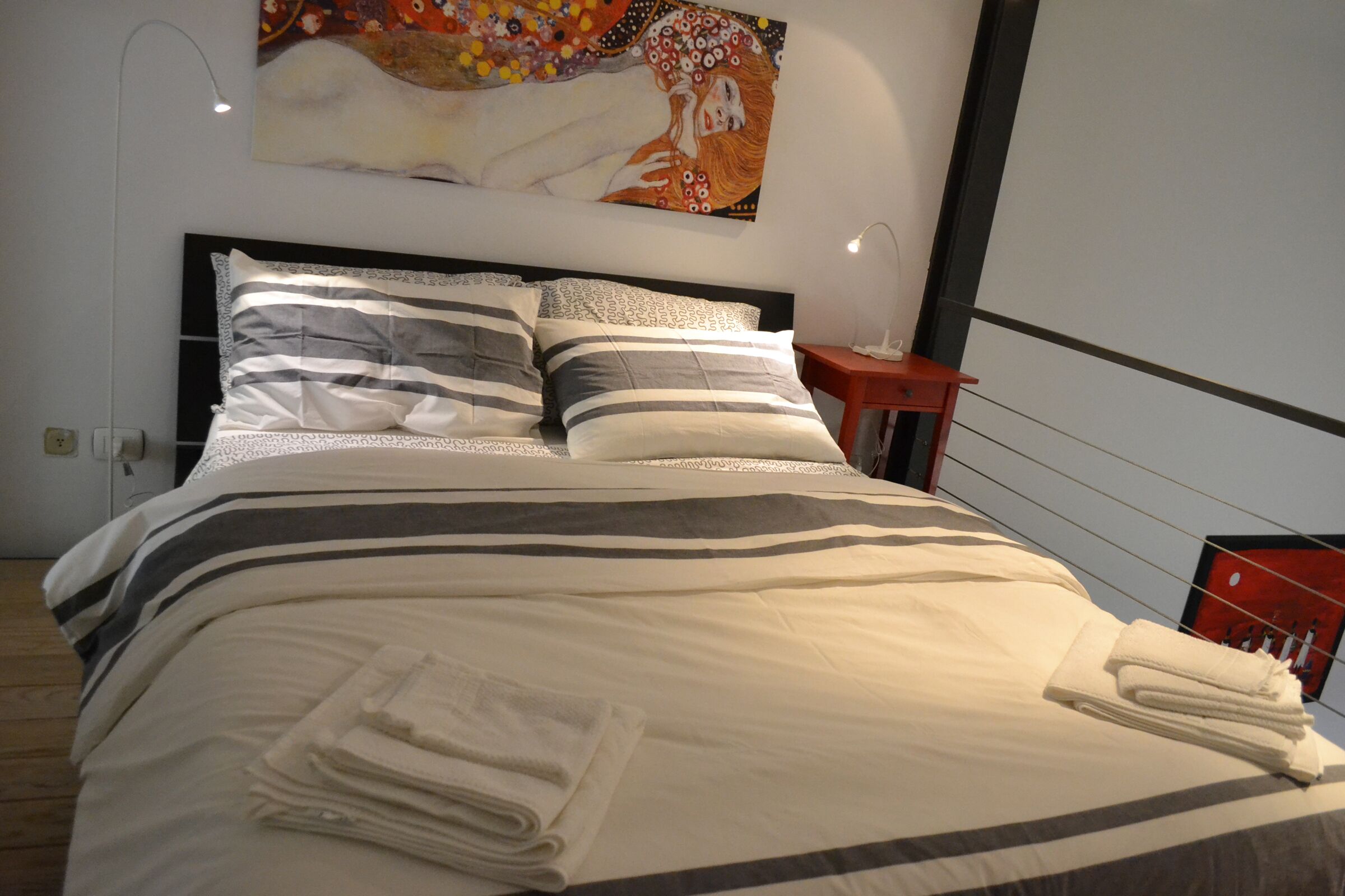 Un lit bien fait, avec une literie à rayures et des oreillers, une serviette pliée posée sur le lit, et un tableau accroché au mur au-dessus.