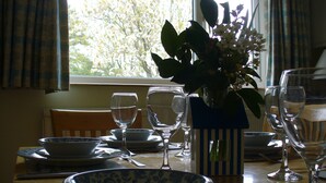 Ein Esstisch ist gedeckt mit Tellern, Schüsseln und Weingläsern, in der Mitte steht eine Blumenvase.