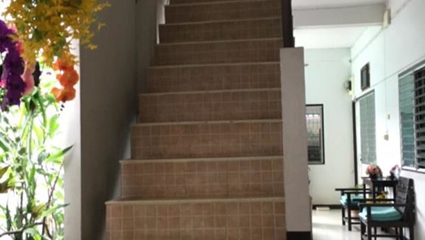 A staircase leading to a second floor, with a potted plant on the left and a dining area with tables and chairs on the right. - Ampawan Guesthouse (Chiang Mai)